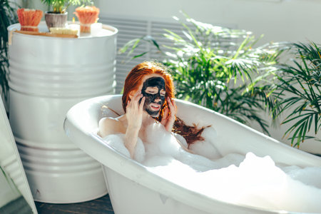 Young beautiful red-haired girl making a clay face mask for beauty during spa treatments in the...