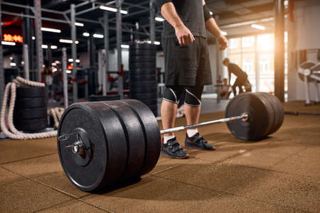 Heavy beautiful barbell on floor of gym, male legs standing near bar, bodybuilder practicing for training, active people, professional sport conceptの写真素材