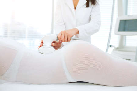Close up of female doctor hands holding a modern medical equipment for body skin massage and treatment. Focus on therapist beautician s hands making LPG treatment to female butt at beauty SPA clinic.の写真素材