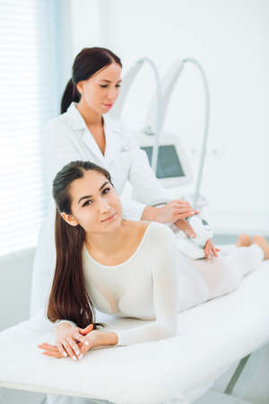 Lymphatic drainage massage LPG apparatus process. Pleased caucasian woman smiling at camera on a massage table getting a lpg massage on her bodyの写真素材