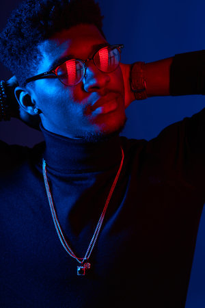 Photo of intelligent serious man of african ethnicity wears dark poloneck sweater and glasses,...