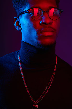 Low key studio shot of young handsome African man in glasses wearing smart poloneck with amulet on...
