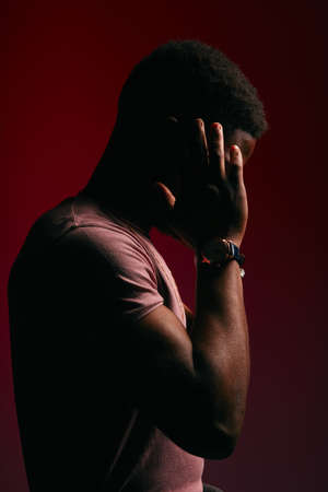 Unrecognizable African male model with athletic body dressed in casual t-shirt posing on dark red background in profileの写真素材