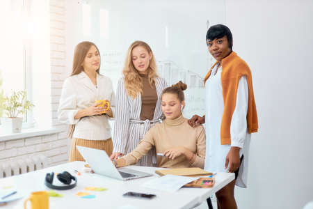 Four diverse colleagues, co-workers stand together in office, hug each other. caucasian and african partnershipの写真素材