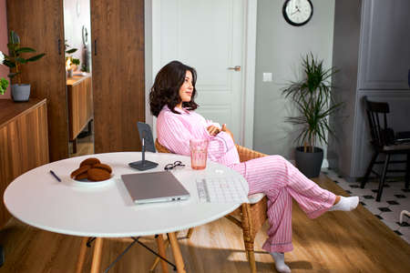 expectant mother, pregnant woman tenderly embracing and stroking her tummy while sitting on chair at home, 9 months pregnant woman awaiting babyの写真素材