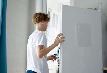 rear view on young caucasian boy open the fridge looking for something to eat, in the kitchen at homeの写真素材