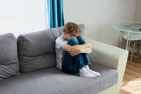 sad child boy sit crying alone at home. school boy suffer from autismの写真素材