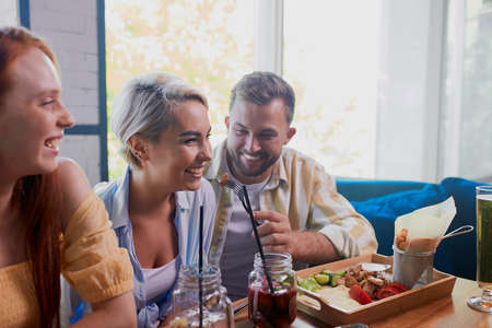 beautiful caucasian men and women hold friendly meeting in cafe, they have a great time after work, have talk. leisure, drinks, people and communication conceptの写真素材
