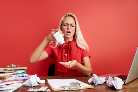 young blonde sad and depressed caucasian manager working in stress at office computer desk feeling overwhelmed and frustrated suffering headache and depression isolated over red background.の写真素材