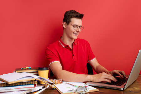 caucasian man is concentrated on work in the office, studio shoot. young male sit alone isolated over red backgroundの写真素材