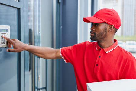 afro american man near intercom with orders, worker of delivery service hold food in cardboard boxesの写真素材
