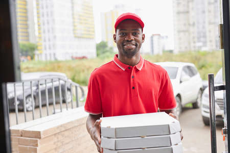 young african black man work in delivery company, came to clients to give it, wearing red uniformの写真素材