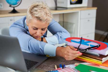 english tutor want to sleep during lesson online, lie on table near book and laptop