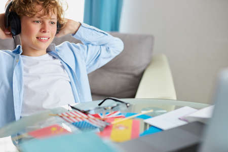 caucasian teen boy sit with laptop, studying online, enjoy education during quarantine. indoorsの写真素材