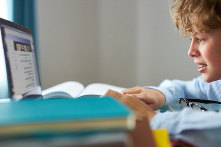 caucasian teen boy sit with laptop, studying online, enjoy education during quarantine. indoors