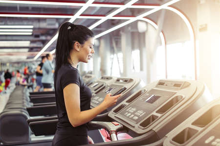 fit Sportswoman using smartphone for training workout app while jogging on treadmillの写真素材