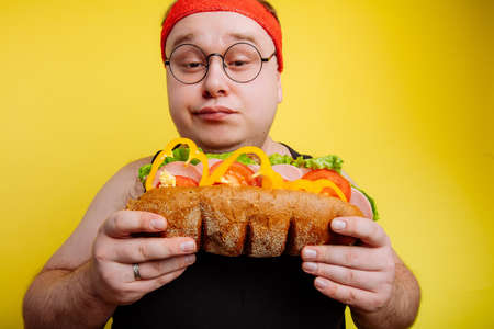 Diet failure of fat man eating fastfood . Happy smile overweight male looking burgerの写真素材