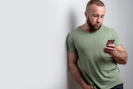 American bearded guy in casual wear chatting on smart phone with friend or girlfriend, looking at...