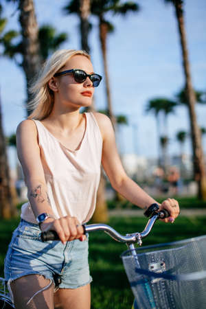 Young active student female riding through the park after colleage classes. Bike as a trendy transport. Healthy outdoors activity on a warm summer day. Bicycle trend in the city.の写真素材