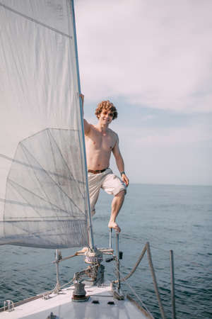 Young hipster man standing on handrail of white yacht against calm blue sea background with copyspace.の写真素材