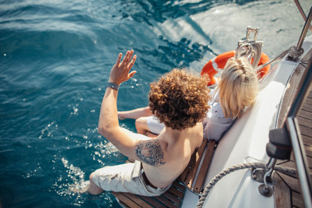 High angle view from the back of unrecognizable man and woman sitting on the feed of modern boat,...