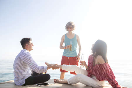 People on yacht drinking beers while talking - Group of friends having party on sailing boatの写真素材