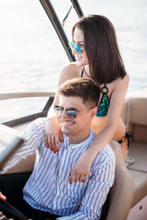 Young married couple having sea excursion on motor boat while spending their honeymoon trip on seaside resort in Thailand, young well groomed husband sitting behind the helm, navigating to the islandの写真素材