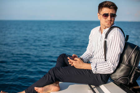 Cheerful european tourist with backpack on sailboat, relaxation in luxury sea boat trip, summertime leisure time on water transport, freedom and enjoyment conceptの写真素材