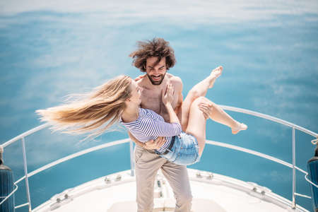 Hot young lovers starting foreplay on the bow of the luxury boat in open sea in summer. Young brunette man holding on hands sensual blonde woman. Outdoor portrait of sea travel recreation lifestyle.の写真素材