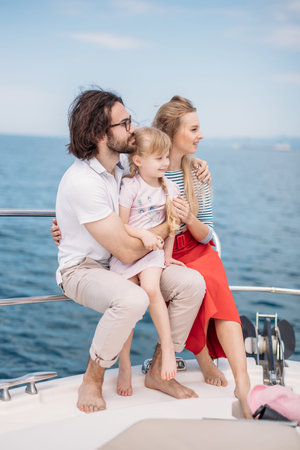 Father, mother and 4-year old daughter sailing on yacht at sunny summer day. Happy family enjoying...