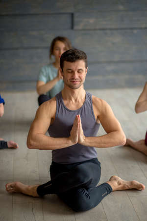 Young sportive male instructor practicing yoga with group of young women in studio over grey background. Training, Flexibility, Well-being Conceptの写真素材