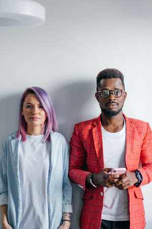 Portrait of serious no emotion face multiracial couple isolated over gray wall background, copy space. African man dressed in red jacket and caucasian woman with dyed violet hair looking at cameraの写真素材