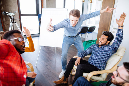 Group of young excited people lifting up their hands in team spirit high five over table, sitting in...