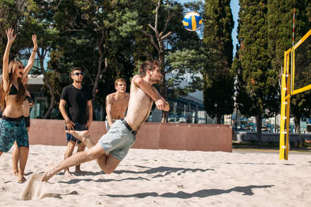 Fit, strong, healthy women and men doing sport on beach. Beach volleyball at vacation leisuretime. Moment when man player with total body stretching out in the air to reach and beat off the ballの写真素材