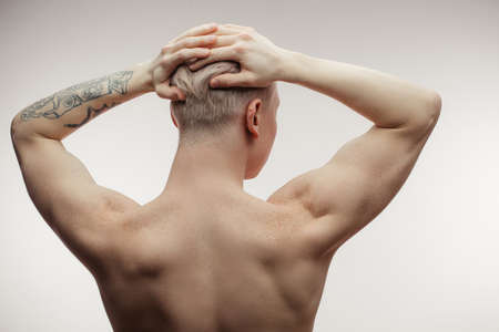 Young blonde man demonstrating his muscular back with perfect freckled skin, straining musculs, tensing arms, isolated over white backgroundの写真素材
