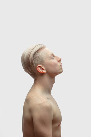 Profile shot of albino shirtless athletic male model with perfect skin and stylish haircut on white...