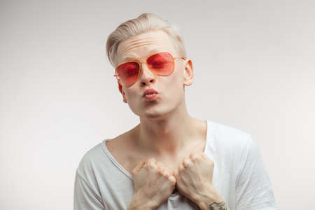 Hipster blonde guy wearing trendy pink sun glasses posing pouting and sending air kiss with pouted lips, full of positive emotions and love love. Human Positive Emotions, Fashion and Beauty Conceptの写真素材