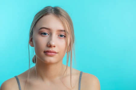 Studio isolated shot of pretty blonde woman with hairbun in grey singlet over blue background. Skin care concept.の写真素材