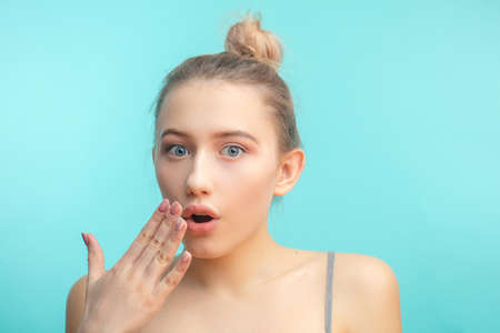 Surprised shoked caucasian girl covers her mouth with hand and keeps her eyes wide open. Casual woman saying wow on a blue background.の写真素材
