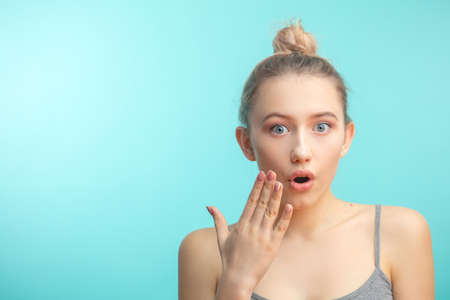 Surprised shoked caucasian girl covers her mouth with hand and keeps her eyes wide open. Casual woman saying wow on a blue background being astonished or horrified by coming news .の写真素材