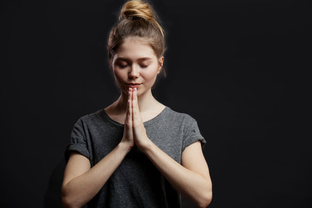 Portrait of peaceful happy european female student in casual clothes, holding palms in pray while...