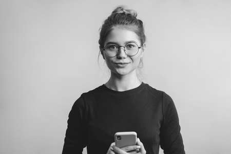 Monochrome shot of portrait of confident pleasant young teacher female holding mobile phone isolated over white backgroundの写真素材