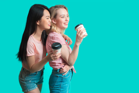 Portrait Couple of multiracial girlfriends looking at camera while holding takeaway coffee cup...