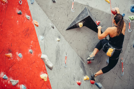 Sporty strong young woman in black outfit exercising in boulder climbing hall reaching new results,...