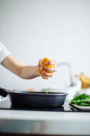 Croped view of female hands squeezing the orange on the frying pan in at kitchen.