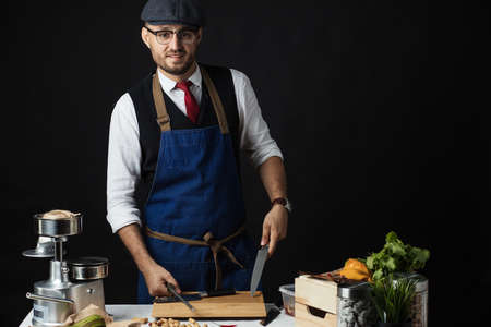 Pleased caucasian chef wearing spectacles and cap looking confidently at the camera and smiling representing professional approach to businessの写真素材
