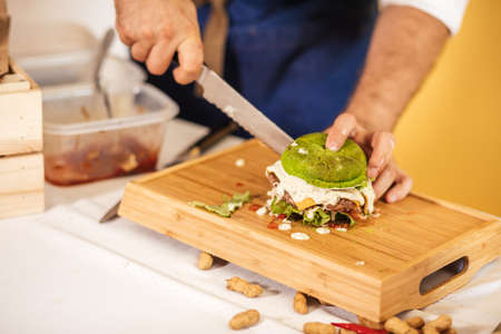 Male hands cuttung fresh self made burger with spinach bun on wooden board, close upの写真素材