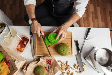 High angle view of Cook s hands cutting green spinach bun on table, isolated on white table with ingridients for burgers . Catering and Good Quality Fastfood conceptの写真素材