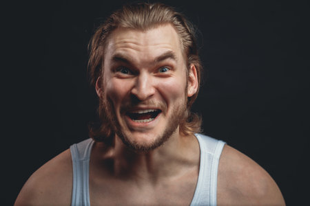 closeup portrait of strong guy with stupid face isolated black background. funny look. madness...