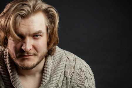 closeup photo of unshaven blond man with long bangs on the black background. copy space